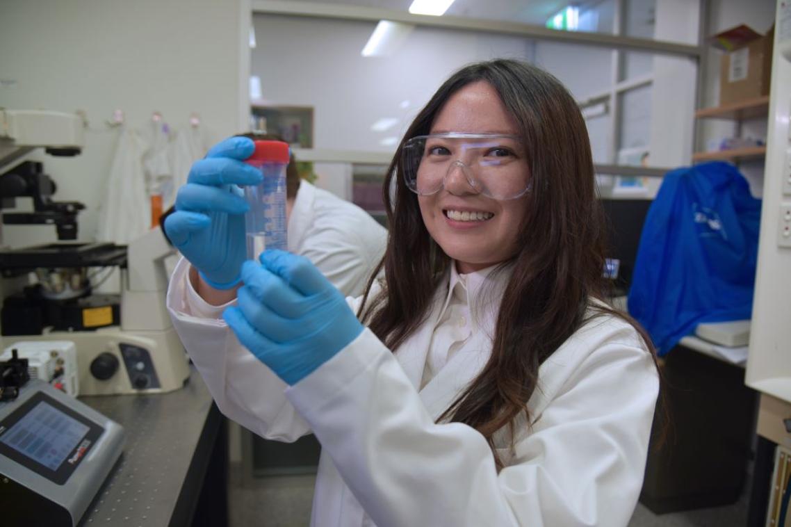 A woman in a lab coat smiling and holding a test tube