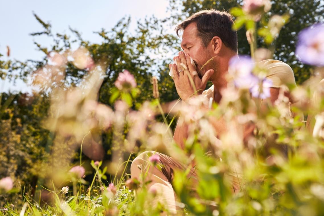 A man sitting in long grass blowing his nose.